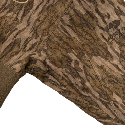 Close-up of MST Youth Eqwader Full Zip Jacket featuring Mossy Oak Bottomland pattern, fleece-lined hem, and MOSSY OAK BOTTOMLAND logo, highlighting waterproof and breathable fabric technology.