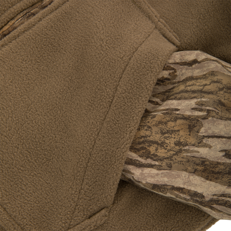 Close-up of the MST Youth Eqwader Full Zip Jacket's textured tan fleece and woodland camouflage fabric, highlighting its innovative dual-zone, moisture-wicking design for optimal comfort in varying conditions.