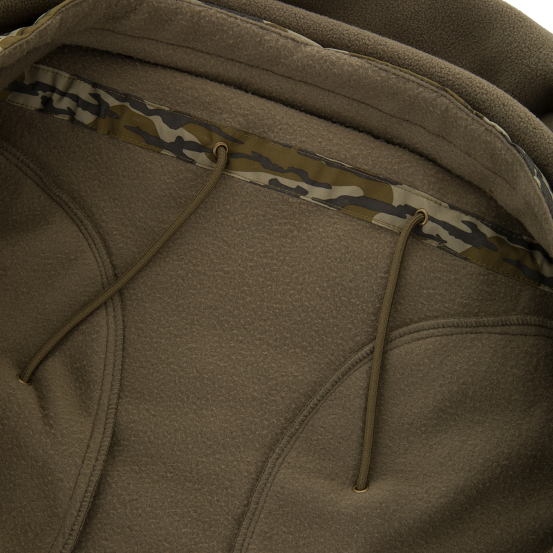 BFCM - MST Camo Eqwader 1/4 Zip Jacket close-up shows textured fleece, camo-patterned hood binding, and drawcords, emphasizing Drake's innovative, breathable waterfowl gear.