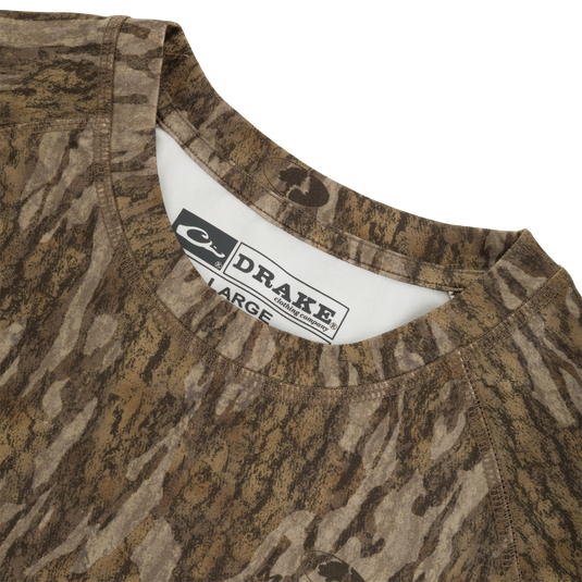 Close-up of the neckline of a brown camouflage Drake Base Layer Crew Neck moisture-wicking shirt showing the interior size label.