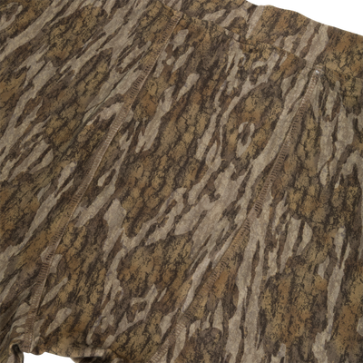 Close-up of Drake Base Layer Bottoms featuring moisture-wicking fabric in a brown and tan tree bark camouflage pattern with visible seams.
