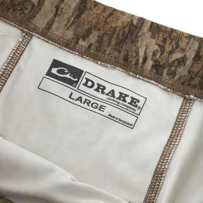 Close-up of the interior of a Waterfowl Drake Base Layer Bottom, showing a printed label that reads DRAKE clothing company, size LARGE, and Made in Bangladesh.