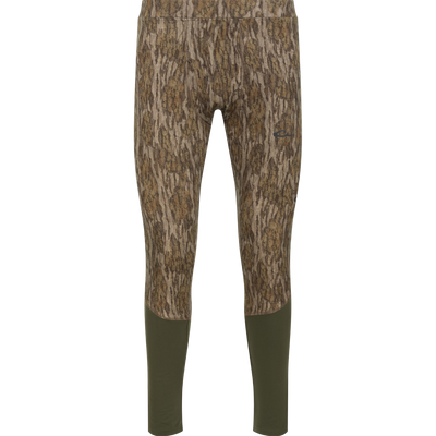 Drake Base Layer Bottom moisture-wicking, full-length leggings featuring a Mossy Oak Bottomland tree bark camouflage pattern on the upper portion and solid dark green lower legs.