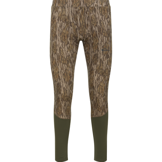 Drake Base Layer Bottom moisture-wicking, full-length leggings featuring a Mossy Oak Bottomland tree bark camouflage pattern on the upper portion and solid dark green lower legs.