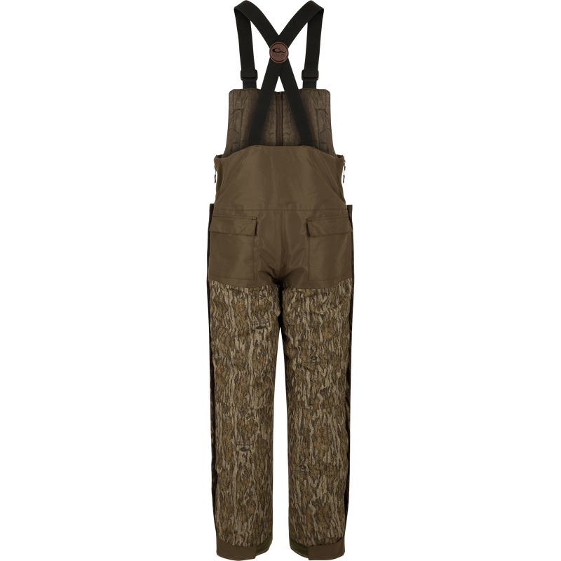 A pair of overalls with straps, perfect for hunters seeking warmth in frigid weather. The Guardian Elite Bibs offer full-body cover-up and protection. Waterproof, windproof, and breathable, with reinforced knees and seat. Features include chest pocket, handwarmer pockets, leg zippers, and ankle closure cuff. From Drake Waterfowl, high-quality hunting gear for big game, waterfowl, turkey, and fishing.