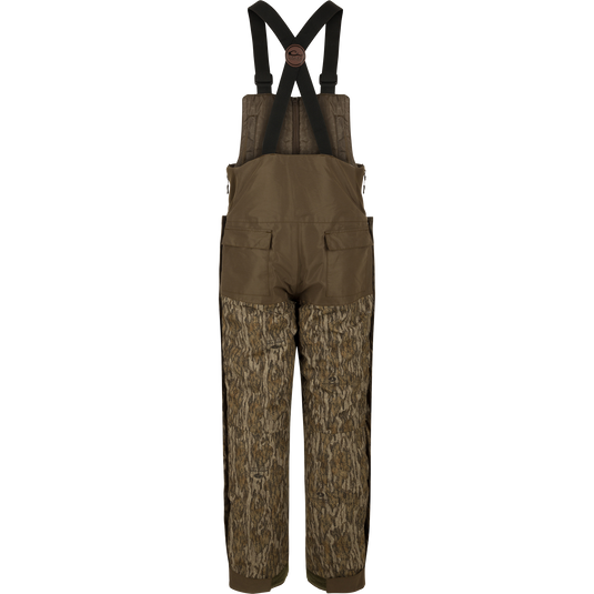 A pair of overalls with straps, perfect for hunters seeking warmth in frigid weather. The Guardian Elite Bibs offer full-body cover-up and protection. Waterproof, windproof, and breathable, with reinforced knees and seat. Features include chest pocket, handwarmer pockets, leg zippers, and ankle closure cuff. From Drake Waterfowl, high-quality hunting gear for big game, waterfowl, turkey, and fishing.