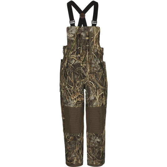 A product image of the EST Guardian Elite™ Bib Shell Weight, featuring a camouflage overalls with straps, perfect for hunters needing protection in any weather conditions. Made with 100% waterproof/windproof/breathable fabric and reinforced knees, seat, and wear areas. Adjustable shoulder straps, chest pockets, and fleece-lined handwarmer pockets provide convenience and comfort. Ideal for use in a ground blind.