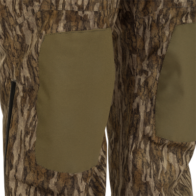 Close-up of MST Waist-High Insulated Bibs, featuring camouflage fabric, heavy-duty elastic suspenders, zippered slash pockets, and cargo pockets for secure storage.