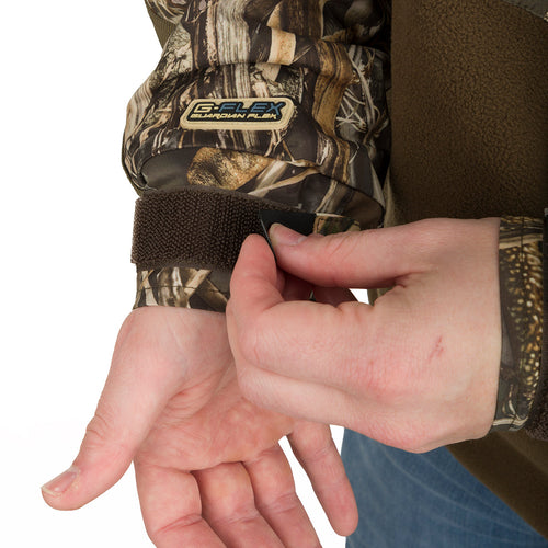 A person wearing MST Guardian Eqwader Flex Fleece 1/4 Zip Jacket - Old School Green, putting on a camouflage wrist band.