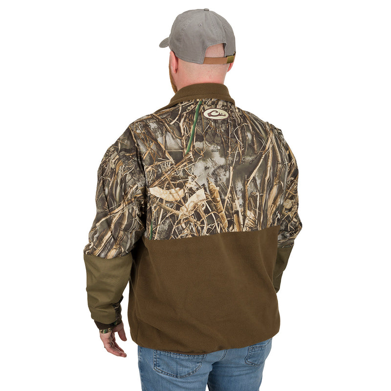 A man wearing the MST Guardian Eqwader Flex Fleece 1/4 Zip Jacket - Old School Green, a camouflage jacket with a hat, showcasing the outdoor style and protection of Drake Waterfowl® gear.