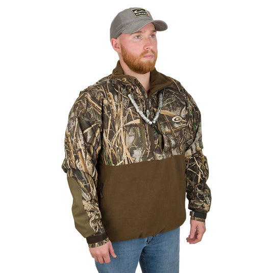 A man wearing a camouflage jacket and hat, part of the MST Guardian Eqwader Flex Fleece 1/4 Zip Jacket - Old School Green collection by Drake Waterfowl.