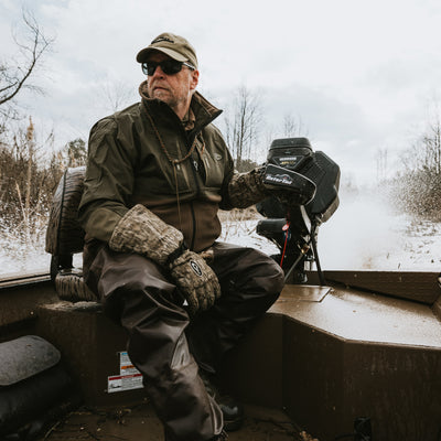 A man in a boat wearing the MST Guardian Eqwader Flex Fleece Full Zip Jacket by Drake Waterfowl, featuring Guardian Flex™ upper body, 350-gram fleece lower body, and HD3 elbow protection.