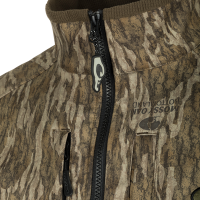 Close-up of the MST Windproof Softshell Jacket featuring camo pattern, high collar, zippered chest pockets, and branded zipper pull, designed for optimal warmth and breathability.