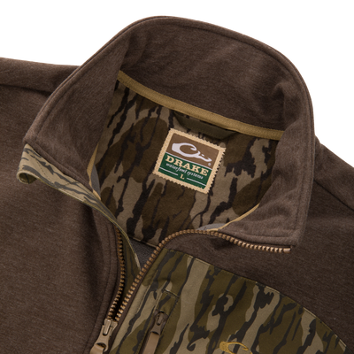 Close-up of the MST Heritage Hybrid Windproof Jacket, highlighting the sturdy brown outer fabric, camo-patterned lining, Drake label, and zipper, showcasing durable outdoor design.
