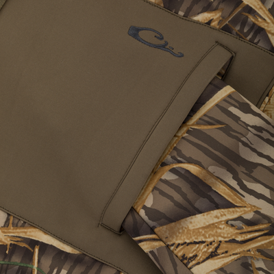 Close-up of an olive green Slacker Quarter Zip Hoodie with High Handwarmer Pockets fleece quarter-zip pocket with a small embroidered logo, layered over a camouflage pattern.