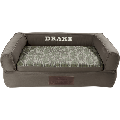 Team Gun Dog Landing Zone Premium Canvas Dog Couch with olive-drab cover, camouflage cushion, and embroidered DRAKE branding, featuring three-sided bolster and slip-resistant bottom.