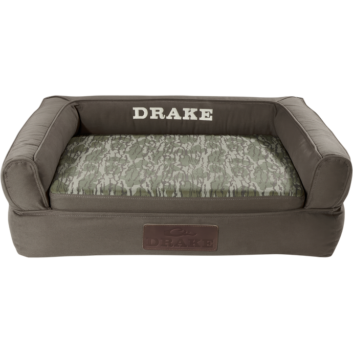 Team Gun Dog Landing Zone Premium Canvas Dog Couch with olive-drab cover, camouflage cushion, and embroidered DRAKE branding, featuring three-sided bolster and slip-resistant bottom.