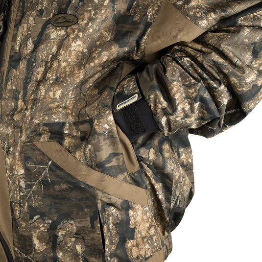 A person wearing the LST Reflex 3-in-1 Plus 2 Jacket - Realtree, a versatile solution for all hunting conditions. Waterproof, windproof, and breathable G3-Flex™ fabric with adjustable cuffs and removable hood. Includes a synthetic down pack jacket with adjustable waist and removable sleeves. Stay warm, dry, and comfortable.