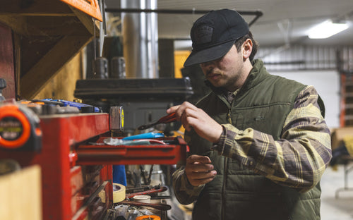 Man in workshop wearing Delta Featherless Down Vest, checking tools in a red toolbox, highlighting its lightweight warmth and water-resistant features for versatile outdoor use.