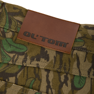 Throwback 80 Field Pant close-up featuring a brown leather label on durable camouflage cotton twill, highlighting reinforced stitching and antique brass details for rugged functionality.