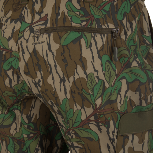 Ol' Tom Tech Stretch Turkey Pants featuring a close-up of camouflage fabric with zipper details, highlighting the hidden stretch waistband and large cargo pockets for hunting functionality.