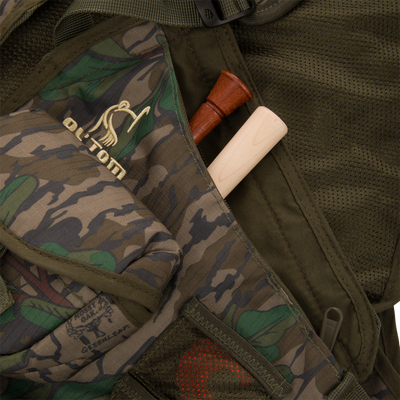 Youth Time and Motion Turkey Vest featuring a camouflage pattern, wooden stick in pocket, and multiple pouches for hunting essentials.