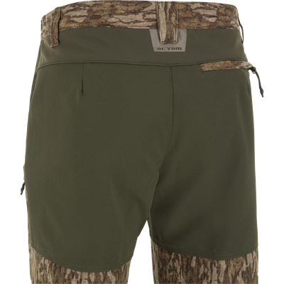 Ol' Tom Early Bird SWT Pant, featuring olive technical fabric with camo panels, reinforced knees, zip pockets, and insect-repellent technology for warm-weather hunting comfort.