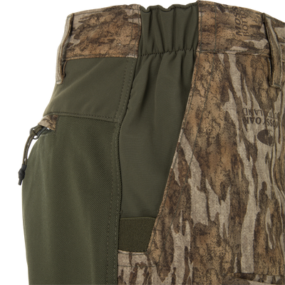 Ol' Tom Early Bird SWT Pant waistband close-up, showcasing Mossy Oak “Bottomland” camo, olive-green stretch panel with zipper, and elasticized section for mobility.