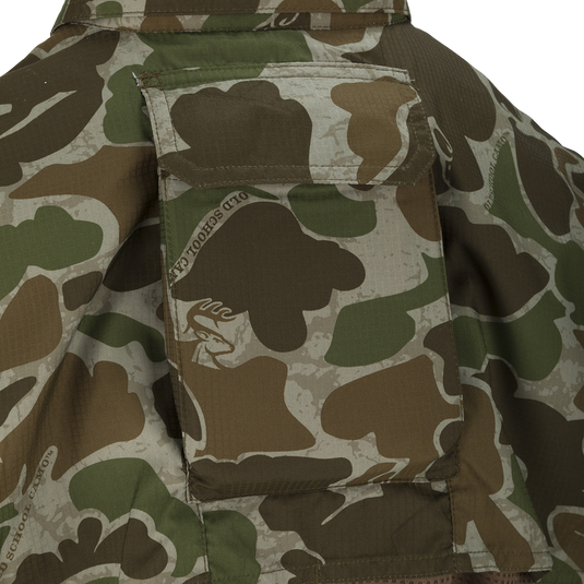 A close-up of the Youth Mesh Back Flyweight Shirt 2.0, a camouflage jacket with a logo patch and large chest pockets.