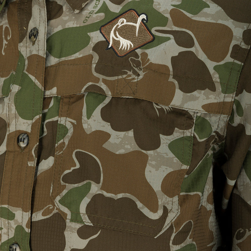 A close-up of the Women's Mesh Back Flyweight Shirt 2.0, featuring a camouflage pattern. The shirt has a button-down collar, mesh back panel, and two large chest pockets. Made with lightweight, breathable polyester for comfort during outdoor activities.
