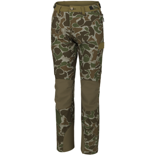 A pair of Women's Tech Stretch Turkey Pants, featuring a camouflage pattern. Designed for spring turkey hunting, these lightweight, moisture-wicking pants have reinforced knees, relaxed fit, and adjustable waistband for comfort. Includes mesh and zippered pockets for ventilation and storage.