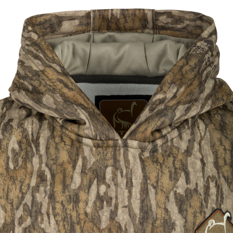 Ol' Tom Youth Camo Performance Hoodie: A close-up of a jacket with a logo. Soft, combed fleece interior for comfort and heat retention. Double-lined hood for wind protection. Kangaroo pouch for extra warmth.
