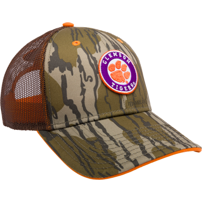 Clemson Bottomland Mesh Back Cap with Mossy Oak Camo pattern. Structured trucker cap with embroidered college logo, mesh panels, and snap-back closure. Ideal for hunting and outdoor enthusiasts.