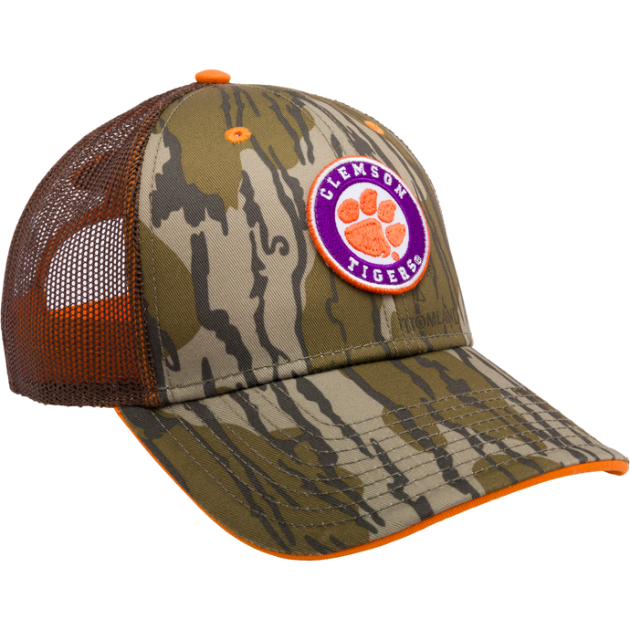 Clemson Bottomland Mesh Back Cap with Mossy Oak Camo pattern. Structured trucker cap with embroidered college logo, mesh panels, and snap-back closure. Ideal for hunting and outdoor enthusiasts.