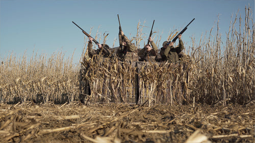 A group of men in camouflage holding guns, using the Ghillie 4-Man Blind with No-Shadow Dual Action Top from Drake Waterfowl for hunting in various outdoor settings.