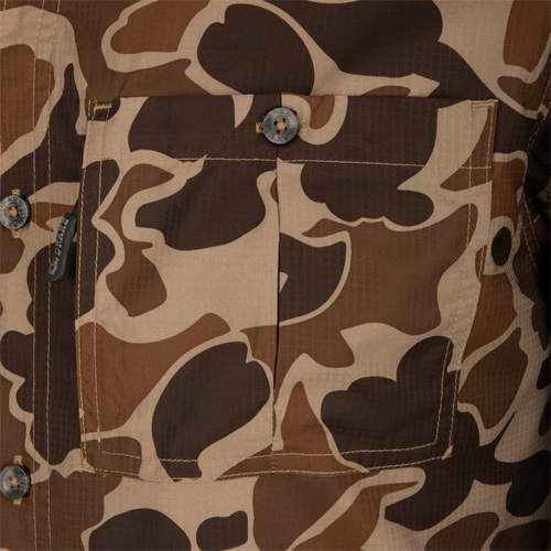 A close up of the 8-Shot Flyweight S/S Shirt's pocket and button details, featuring a hidden zipper and button-through chest pocket with a hidden vertical zipper. The lightweight Dobby fabric showcases the exclusive Old School Camo pattern. Classic fit with a hidden button-down collar and vented cape back.