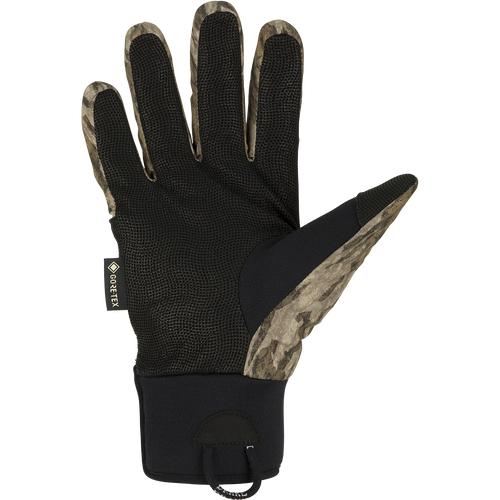 A black glove with a camouflage pattern, perfect for early season waterfowl hunting. Made with waterproof Refuge HS™ shell fabric and GORE-TEX® membrane for 100% waterproof/breathable protection. Features include a digitized goat skin leather palm and gusseted neoprene cuffs. Stay-Put™ liner system ensures no twisting or bunching. Adjustable gusset Velcro cuff closure and pull loop assist for easy use. From Drake Waterfowl, your go-to store for high-quality hunting gear and clothing.