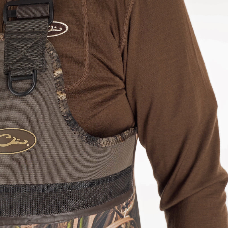 A person wearing a brown shirt, standing outdoors with a logo on their chest, showcasing the Buckshot Eqwader 1600 Neoprene Wader 3.0.