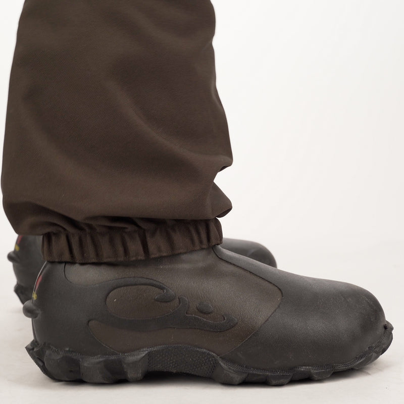 Buckshot Eqwader 1600 Neoprene Wader 3.0: A close-up of a person's legs wearing black boots, showcasing the durable construction and waterproof features of these hunting waders.
