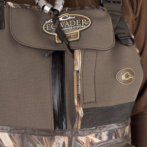 A close-up of the Buckshot Eqwader 1600 Neoprene Wader 3.0, featuring a bag, camouflage vest, logos, metal ring, label, black leather belt, rope, and fabric.