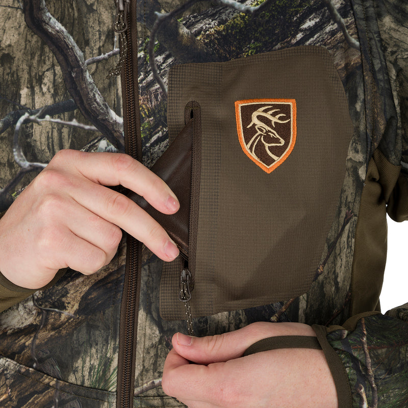 A person putting a wallet in the vertical zippered chest pocket of the Pursuit Full Zip Hoodie with Agion Active XL, a lightweight and breathable performance jacket from Drake Waterfowl.