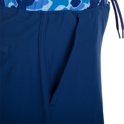 A close-up of the Youth Commando Lined Volley Short 5, a versatile blue and white fabric short with a scalloped hem, elastic waistband, and adjustable drawstring. Features include quick-drying, moisture-wicking, and a built-in interior comfort liner.
