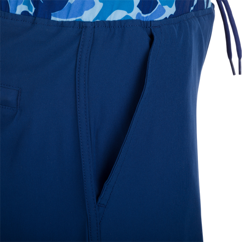 A close-up of the Youth Commando Lined Volley Short 5, a versatile blue and white fabric short with a scalloped hem, elastic waistband, and adjustable drawstring. Features include quick-drying, moisture-wicking, and a built-in interior comfort liner.
