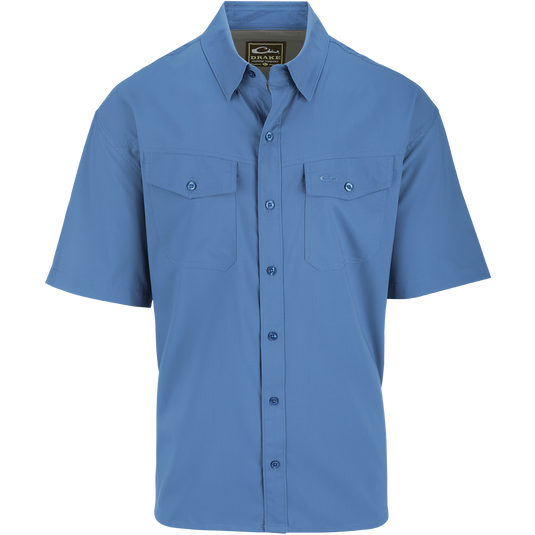 A blue button-up shirt with hidden button-down collar and two chest pockets with button-through flaps. Made of 100% Polyester textured dobby fabric, it features UPF30 sun protection and moisture-wicking properties. The shirt has a split tail hem for versatile styling. Perfect for the Traveler's Solid Dobby Shirt S/S.