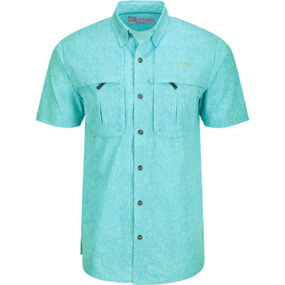 Heritage Heather Shirt S/S: A close-up of a blue shirt with pockets, featuring a logo. Lightweight, moisture-wicking, and quick-drying fabric for comfort. Hidden button-down collar and vented cape back for ventilation. Perfect for outdoor activities or office wear.