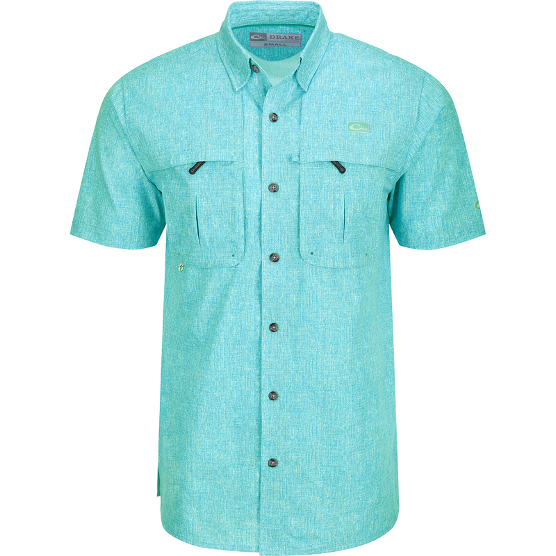 Heritage Heather Shirt S/S: A close-up of a blue shirt with pockets, featuring a logo. Lightweight, moisture-wicking, and quick-drying fabric for comfort. Hidden button-down collar and vented cape back for ventilation. Perfect for outdoor activities or office wear.