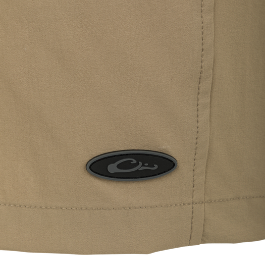 Dock Short 6" - A close-up of the logo on tan shorts made from durable 90% Nylon/10% Spandex fabric. Features include water resistance, quick drying, elastic waist, belt loops, drawstring, mesh lining, front and back pockets, and a bonus pliers pocket.