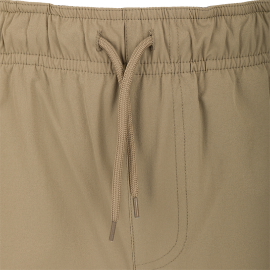 Dock Short 6" - A close-up of khaki shorts made from durable 90% Nylon and 10% Spandex fabric. Features include a water-resistant DWR finish, elastic waist with drawstring, and multiple mesh-lined pockets, including a bonus pliers pocket. Perfect for transitioning from boat to dock.