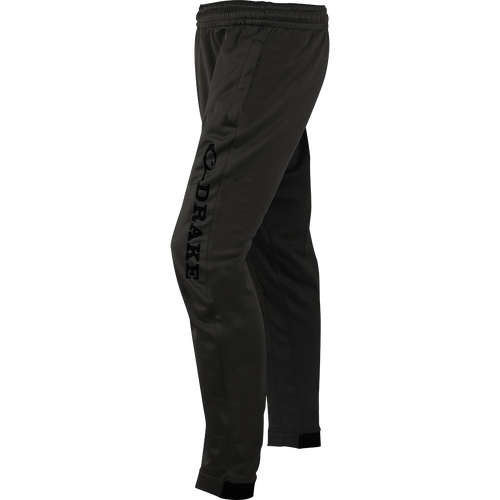 A close-up of the MST Fleece Wader Pant, a pair of black pants with a logo. Ideal for wearing under waders. Warm, comfortable, and durable. Front handwarmer pockets, elastic waist, and snug fit tapered ankles.