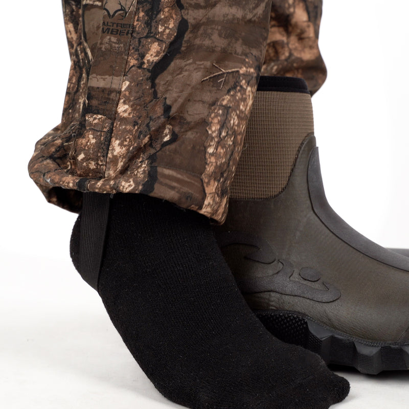 MST Jean Cut Wader Pant: A pair of boots and socks on a foot wearing water-resistant and windproof pants with adjustable waist and ankle.